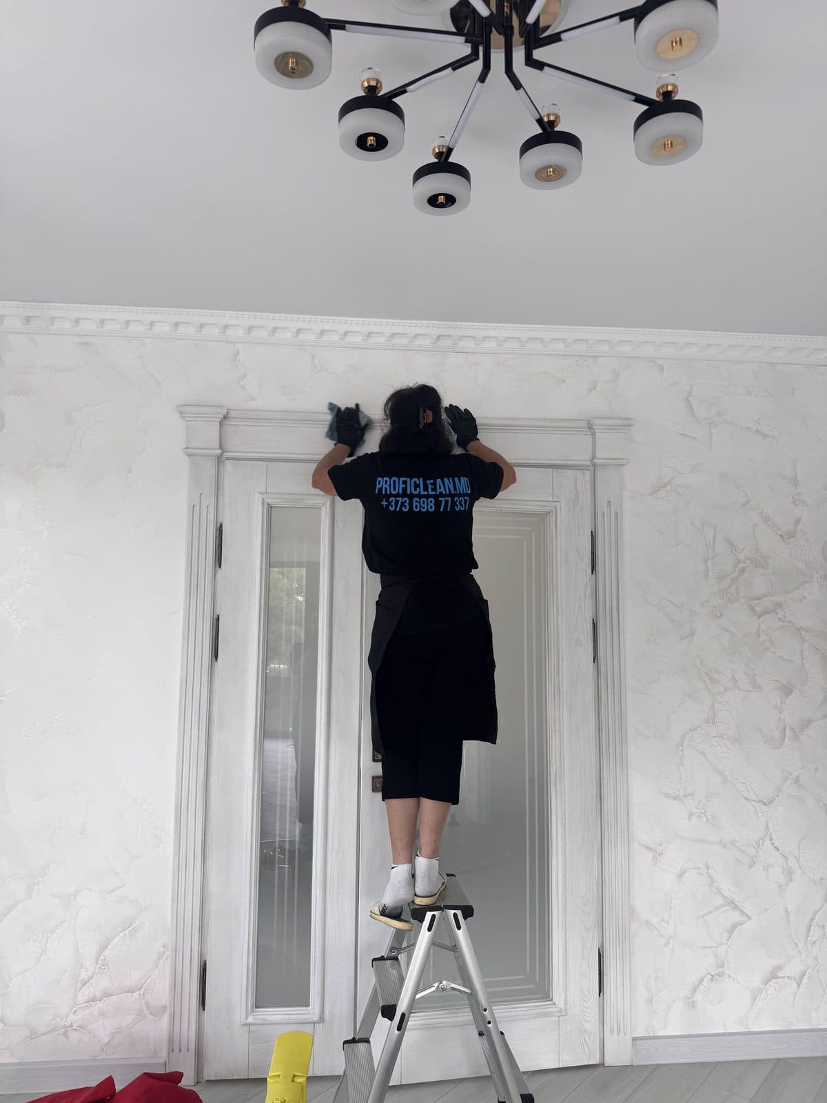 Colegă ProfiClean, de pe scară, șterge ușa și tocul de sus