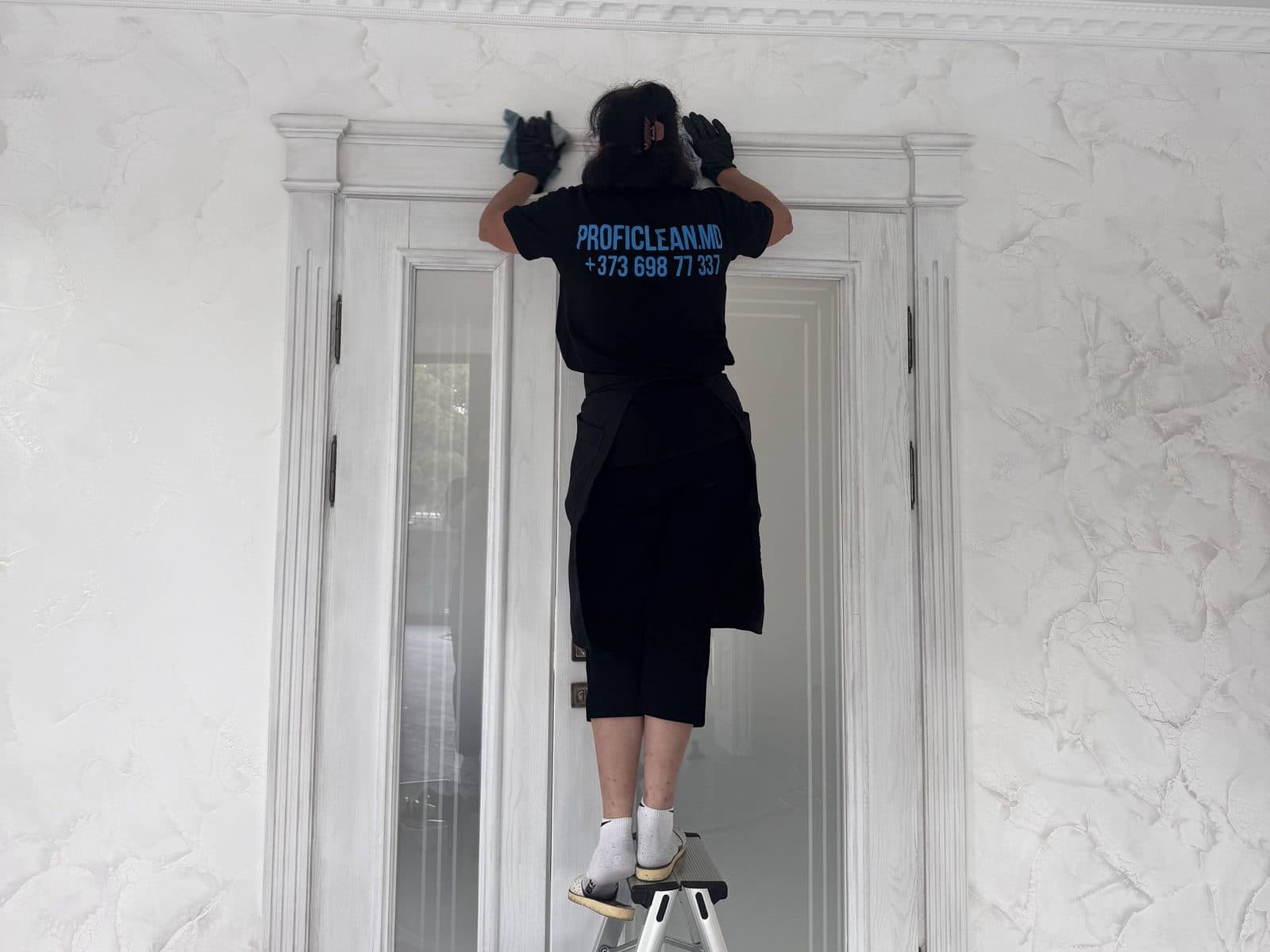 Сотрудница ProfiClean протирает дверь и наличники сверху, со стремянки